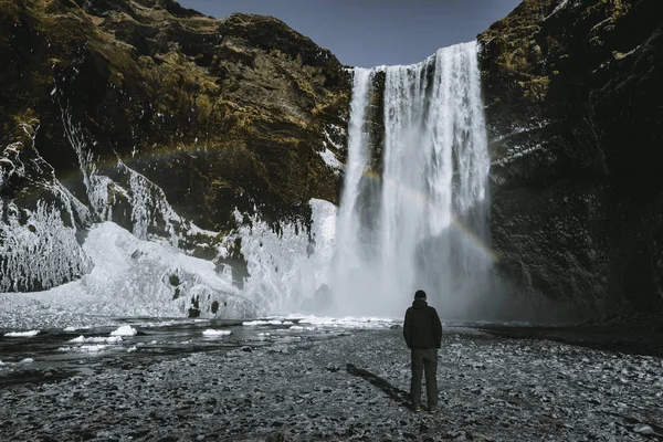 Uma pessoa admira a beleza da cachoeira Skogafoss com arco-íris localizado na Islândia . — Fotografia de Stock