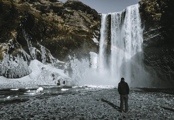 Una persona admira la belleza de la cascada de Skogafoss con arco iris situado en Islandia . — Foto de Stock