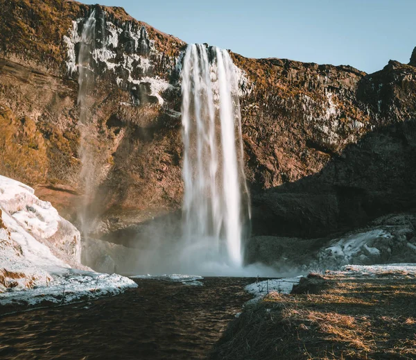 Maravilhosa paisagem de Seljalandsfoss Cachoeira na Islândia em um dia claro com céu azul e neve . — Fotografia de Stock