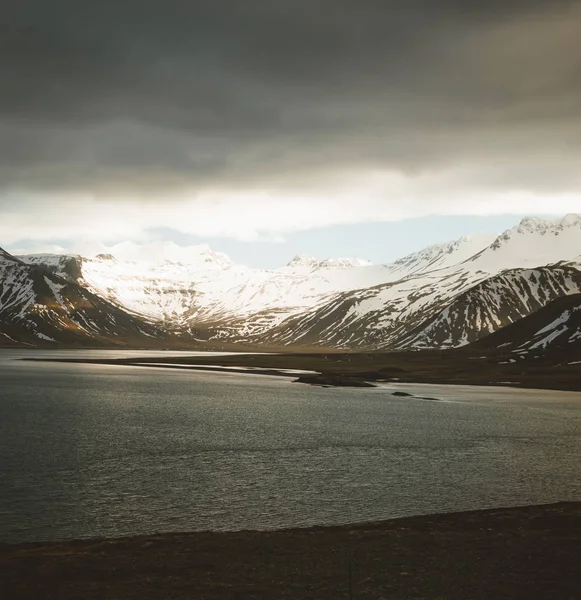 Islands dramatiska himlen med snö utjämnade berget vid sjön havsvatten. Södra sidan om landet. — Stockfoto