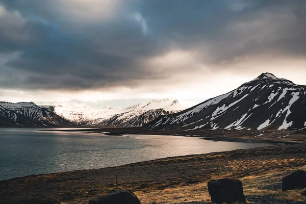 Islands dramatiska himlen med snö utjämnade berget vid sjön havsvatten. Södra sidan om landet. — Stockfoto