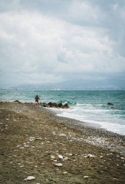 Ada Girit tipik plaj sahne. Plaj boyunca yürüyen genç kimliği belirsiz kadın. Okyanus doğru görüntüleyin. Bulutlu bir günde arka planda ile dağlar.