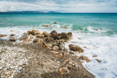 Dalgalar taşlar karşı Girit, Yunanistan'ın güneşli bir günde yendi. Mavi deniz okyanus ön planda arka plan ve taş Beach.