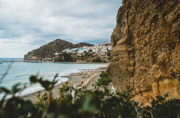 Creta, Grécia. Vista de penhascos para aldeia com embarcações marinhas, barcos e farol. Vista de penhasco na Baía com praia e arquitetura - resort de destino de férias com água do mar clara. Retimno. — Fotografia de Stock