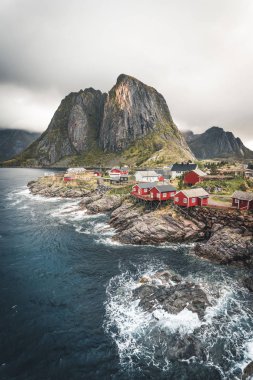 Bulutlar ve mavi gökyüzü ve okyanus dalgaları ile sonbaharda ünlü turistik cazibe Hamnoy balıkçı köyü Lofoten Adaları Reine, Norveç kırmızı rorbu ile Panorama Evleri.
