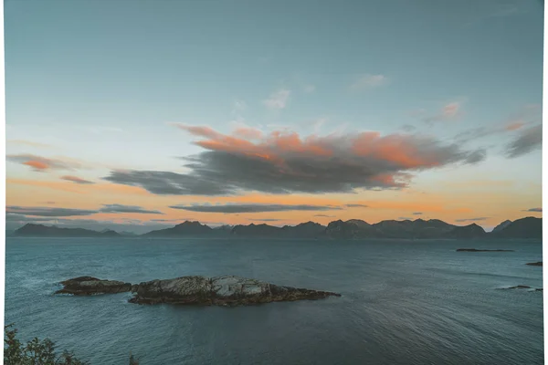 Nascer e pôr do sol em Henningsvaer sobre o oceano atlântico com nuvens cor-de-rosa. A aldeia piscatória localizada em várias pequenas ilhas no arquipélago Lofoten, Noruega sobre um céu azul com nuvens . — Fotografia de Stock