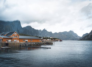 Arka planda dağlar ile bulutlu bir günde Sakrisoy balıkçı köyü sarı rorbu ev sahipliği yapmaktadır. Lofoten Adaları, Norveç