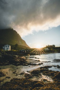 Geleneksel kırmızı asmadan evde Reine Lofoten, Norveç'te yakınındaki Bjoernsand kırmızı rorbu ile ev sahipliği yapmaktadır. Bulutların üstünde bir kumsalı ile günbatımı öğleden sonra.