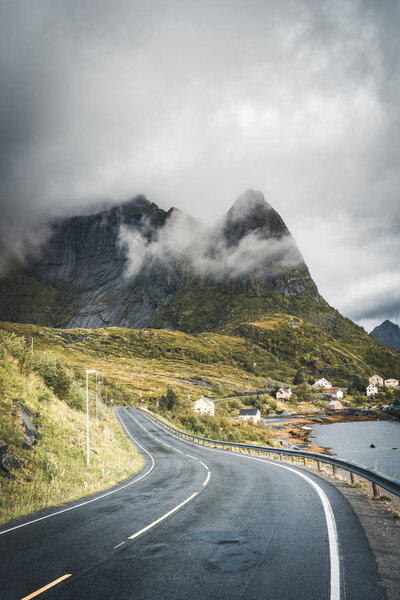 Winding road trip towards Reinebringen in Reine on Lofoten Islands with mountains in the background. Cloudy and moody sky with atlantic ocean.