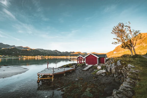 Traditionell röd fishin hus i Bjoernsand nära Reine i Lofoten, Norge med röda rorbu hus. Solnedgången eftermiddag med moln på en sandstrand. — Stockfoto