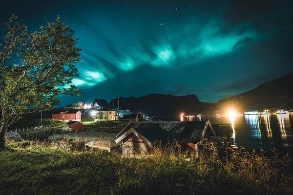 Aurora sobre a tradicional casa de pescadores vermelhos na Noruega, ilhas Lofoten. Luzes do norte nas ilhas Lofoten, Noruega. Céu estrelado com luzes polares. Paisagem noturna com aurora boreal verde, rochas — Fotografia de Stock