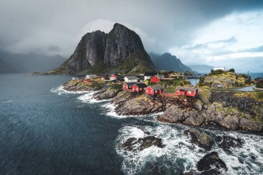 Bulutlar ve mavi gökyüzü ve okyanus dalgaları ile sonbahar günbatımı ünlü turistik cazibe Hamnoy balıkçı köyü Lofoten Adaları Reine, Norveç ile kırmızı rorbu Panoraması evler.