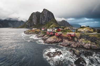 Bulutlar ve mavi gökyüzü ve okyanus dalgaları ile sonbahar günbatımı ünlü turistik cazibe Hamnoy balıkçı köyü Lofoten Adaları Reine, Norveç ile kırmızı rorbu Panoraması evler.