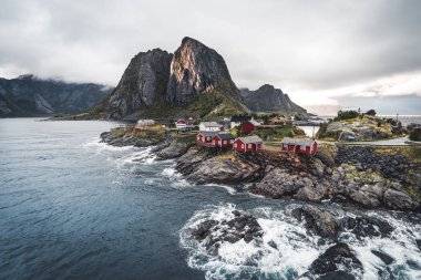 Bulutlar ve mavi gökyüzü ve okyanus dalgaları ile sonbahar günbatımı ünlü turistik cazibe Hamnoy balıkçı köyü Lofoten Adaları Reine, Norveç ile kırmızı rorbu Panoraması evler.
