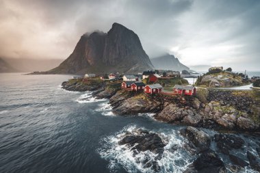 Bulutlar ve mavi gökyüzü ve okyanus dalgaları ile sonbahar günbatımı ünlü turistik cazibe Hamnoy balıkçı köyü Lofoten Adaları Reine, Norveç ile kırmızı rorbu Panoraması evler.