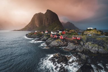 Bulutlar ve mavi gökyüzü ve okyanus dalgaları ile sonbahar günbatımı ünlü turistik cazibe Hamnoy balıkçı köyü Lofoten Adaları Reine, Norveç ile kırmızı rorbu Panoraması evler.
