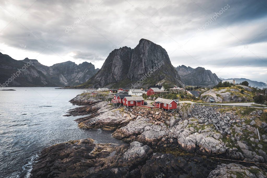 Panorama of famous tourist attraction Hamnoy fishing village on Lofoten Islands near Reine, Norway with red rorbu houses in autumn with clouds and blue sky and ocean waves.