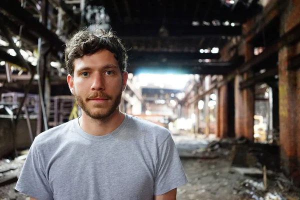 Attractive young man standing outdoor in front of abandoned house, looking at camera. Photo taken in Detroit, Michigan, USA.