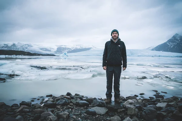 Jonge man staan voor Fjallsarlon ijsberg lagune aan de zuidkant van de gletsjer de Vatnajokull, met drijvende ijsbergen die vanaf de rand van de gletsjer kalven. Fjallsarlon ijsberg lagune op de — Stockfoto