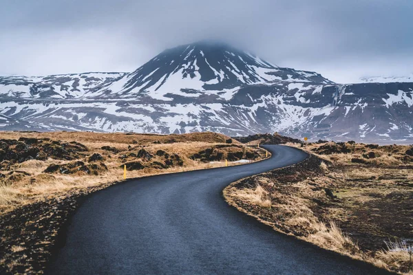 Perspective winding road in Iceland with snow mountain range background on cloudy day autumn season Iceland.