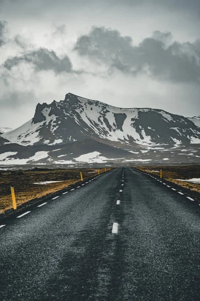 Perspectief van de kronkelende weg in IJsland met sneeuw bergketen achtergrond op bewolkte dag herfst seizoen IJsland. — Stockfoto