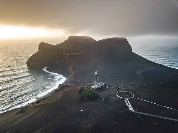カペリーニョス火山、ファリアル島の西海岸のポンタ・ドス・カペリンホスの灯台、劇的な夕日と強い波と雲を持つポルトガルのアゾレス諸島の灯台を見渡します。最後の火山噴火は — ストック写真