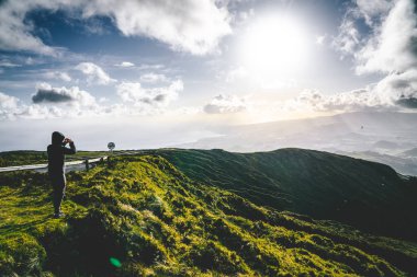 Genç adam turist Lagoa do Fogo, Ateş Gölü, Sao Miguel Adası, Azores, Portekiz güzel panoramik görünümüne bakan. Mavi gökyüzü ve bulutlar ile güneşli bir gün.