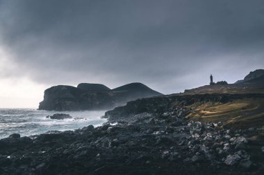 Capelinhos yanardağı, Faial adasında batı kıyısında Ponta dos Capelinhos deniz feneri, Azores, Portekiz dramatik bir gün batımı ve güçlü dalgalar ve bulutlar ile görünümü. Son yanardağ patlaması oldu