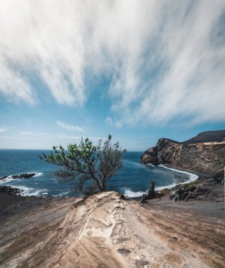 Capelinhos yanardağı, Faial adasında batı kıyısında Ponta dos Capelinhos deniz feneri, Azores, Portekiz mavi gökyüzü ve bulutlar ve dalgalar ile güneşli bir günde görünümü. Son yanardağ patlaması 1957 yılında oldu