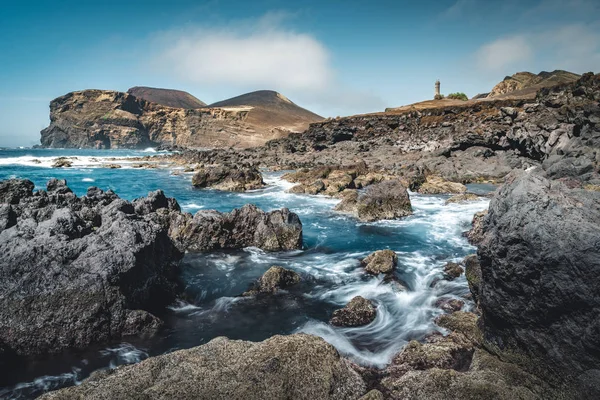 Blick über den Vulkan Capelinhos, Leuchtturm von Ponta dos Capelinhos an der Westküste der Insel Faial, Azoren, Portugal an einem sonnigen Tag mit blauem Himmel und Wolken und Wellen. Letzter Vulkanausbruch war 1957 — Stockfoto