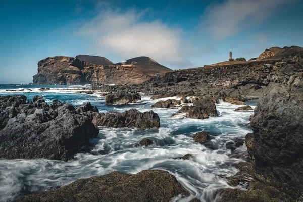 Blick über den Vulkan Capelinhos, Leuchtturm von Ponta dos Capelinhos an der Westküste der Insel Faial, Azoren, Portugal an einem sonnigen Tag mit blauem Himmel und Wolken und Wellen. Letzter Vulkanausbruch war 1957 — Stockfoto