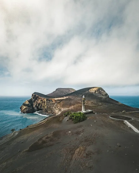 Blick über den Vulkan Capelinhos, Leuchtturm von Ponta dos Capelinhos an der Westküste der Insel Faial, Azoren, Portugal an einem sonnigen Tag mit blauem Himmel und Wolken und Wellen. Letzter Vulkanausbruch war 1957 — Stockfoto