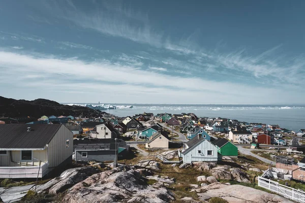 Aerial View of Arctic city of Ilulissat, Greenland. Colorful houses in the center of the town with icebergs in the background in summer on a sunny day with blue sky and clouds — Stock Photo, Image