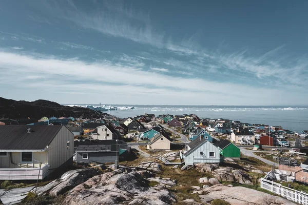 Vista aérea da cidade ártica de Ilulissat, Groenlândia. Casas coloridas no centro da cidade com icebergs no fundo no verão em um dia ensolarado com céu azul e nuvens — Fotografia de Stock