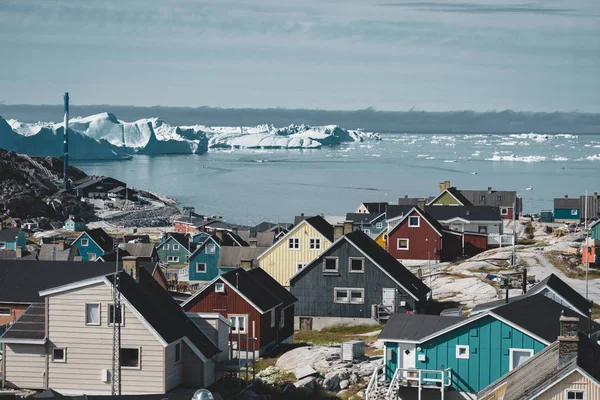 Vista aérea da cidade ártica de Ilulissat, Groenlândia. Casas coloridas no centro da cidade com icebergs no fundo no verão em um dia ensolarado com céu azul e nuvens — Fotografia de Stock