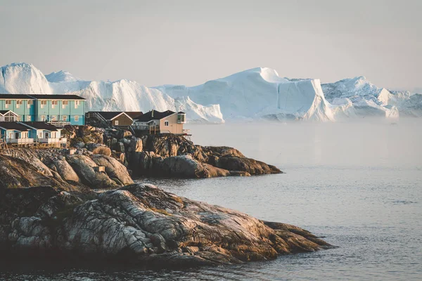 Повітряний вид на арктичне місто Ілуліссат, Гренландія під час заходу сонця з туманом. Кольорові будинки в центрі міста з айсбергами на задньому плані влітку в сонячний день з помаранчевим рожевим — стокове фото