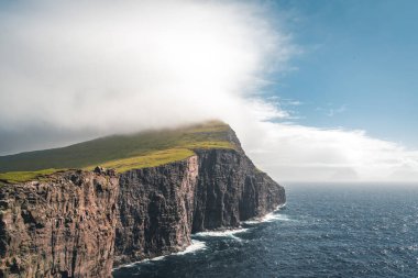 Faroe Adaları Traelanipa. Kölelerin kaya uçurumu okyanusun üzerinde Sorvagsvatn Gölü 'nün yanında yükseliyor. Faroe Adaları 'ndaki vajina adasında bulutlar ve mavi gökyüzü..