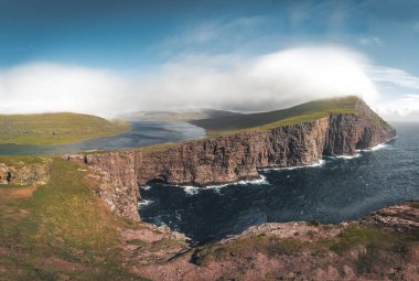 Faroe Adaları Traelanipa. Kölelerin kaya uçurumu okyanusun üzerinde Sorvagsvatn Gölü 'nün yanında yükseliyor. Faroe Adaları 'ndaki vajina adasında bulutlar ve mavi gökyüzü..