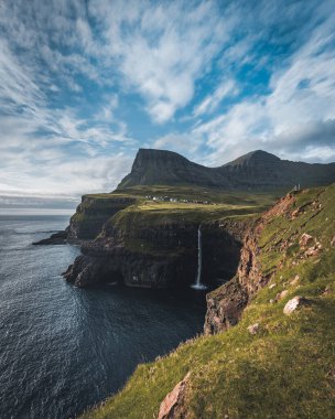 Gasadalur köyü ve Mulafossur 'un ikonik şelalesi, yaz boyunca Bluw Sky ile birlikte. Vagar, Faroe Adaları, Danimarka. Kuzey Atlantik Okyanusu 'nda zor bir durum..