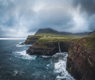 Gasadalur köyü ve Mulafossur 'un ikonik şelalesi Vagar, Faroe Adaları' ndaki hava aracı panoraması. Kuzey Atlantik Okyanusu 'nda zor görünüyor. Yaz boyunca yemyeşil.