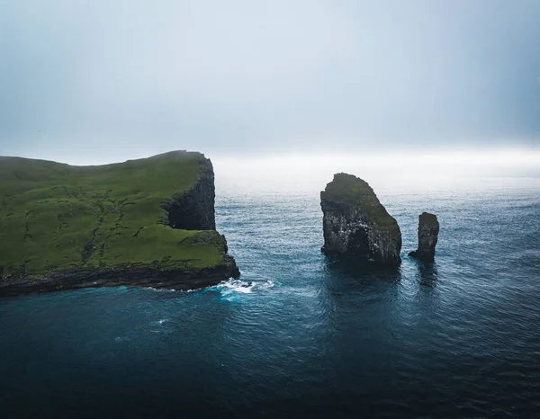フェロー諸島Drangarnir崖とTindholmur島の空中ドローンビュー。大西洋の濃い青色の水と緑豊かな緑と夏の激しい雲の間に撮影。デンマークのフェロー諸島 — ストック写真