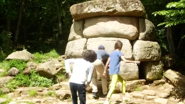 Turisták, felfedezni az ősi dolmen, fényképeket a telefont, a szociális hálózatok. Kilátás a régi épület dolmen fák, 4k között. életlenítés háttér — Stock videók