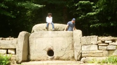 turistler, antik dolmen keşfetmek sosyal ağlar için telefonda fotoğraf çekmek. Antik Bina dolmen ağaçları, 4k arasında bir bakış. arka plan bulanıklık