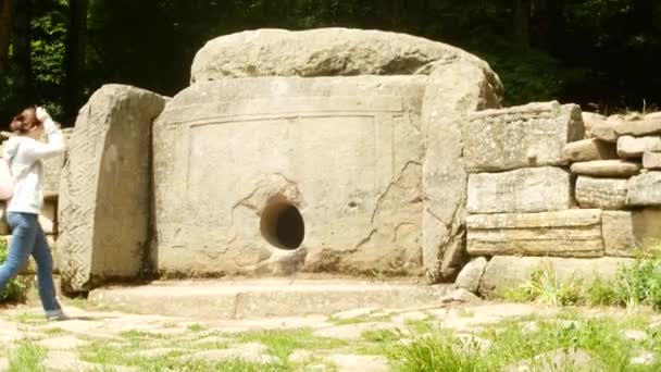 Turister, utforska den antika dolmen, ta foton på telefonen för sociala nätverk. Beskåda av den antika byggnaden dolmen bland träd, 4k. bakgrundsoskärpa — Stockvideo