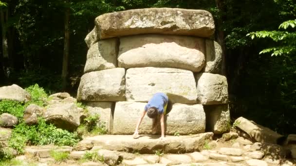 Touristes, explorer l'ancien dolmen, prendre des photos sur le téléphone pour les réseaux sociaux. Vue de l'ancien bâtiment dolmen parmi les arbres, 4k. flou de fond — Video