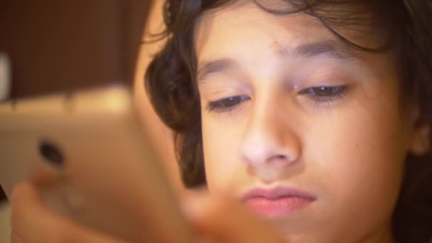 귀여운 십 대는 스마트폰을 사용 하 여 침대에 누워과 밤, 그의 방에 있는 소년. 그는 그의 휴대 전화에서 텍스트를 읽습니다. 눈 가까이 4 k. — 비디오