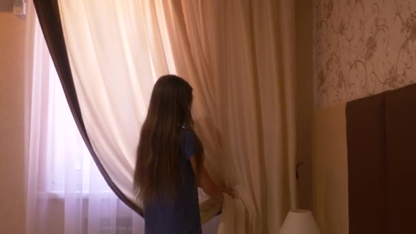 Het meisje wordt de gordijnen op het venster geopend in de ochtend. 4k — Stockvideo