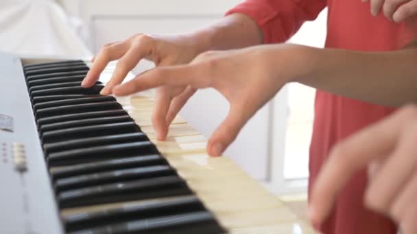 Крупным планом. Играя на пианино в четыре руки. Женские и детские руки играют вместе на синтезаторе. 4k, slow motion — стоковое видео