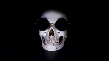 Kafatası siyah bir zemin üzerine yuvarlak güneş gözlüğü. yakın çekim. 4k, dolly shot, defocusing, bulanıklık.