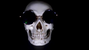 Kafatası siyah bir zemin üzerine yuvarlak güneş gözlüğü. yakın çekim. 4k, dolly shot, defocusing, bulanıklık.